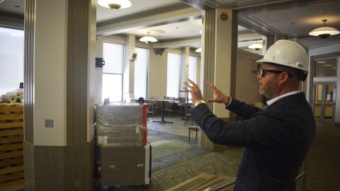 A man in a suit points out various construction work inside of a building.