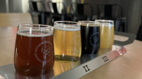 Four small glasses of craft beer arranged in a numbered metal flight tray on a wooden table at Mothfire Brewing Company.