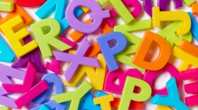 Plastic alphabet letters in all different bright colors are piled on a white background. 