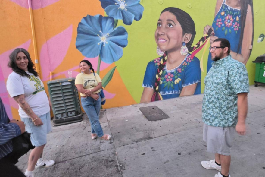 Photo of folks standing against a painted mural of an Indigenous child.