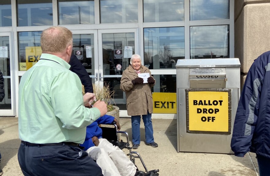 A voter shows her absentee ballot to Franklin County Board of Elections Director Ed Leonard (left) before putting it in the ballot drop box on the last day of weekend early voting before the March 2020 primary. 