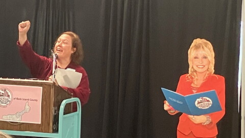 Rock Island Public Library director Angela Campbell, with a cutout of Dolly Parton (at right) announces a $36,205 fundraising campaign to relaunch Dolly's Imagination Library in the county.