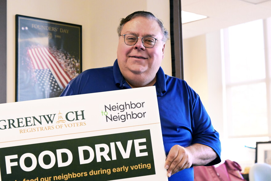 Republican Registrar of Voters Fred DeCaro III holds up a sign promoting a food drive by Neighbor to Neighbor, a local nonprofit that also has a donation bin at Greenwich Town Hall during early voting on October 20th, 2026. DeCaro said he's already received a full bin of donations since the drive commenced on Monday.