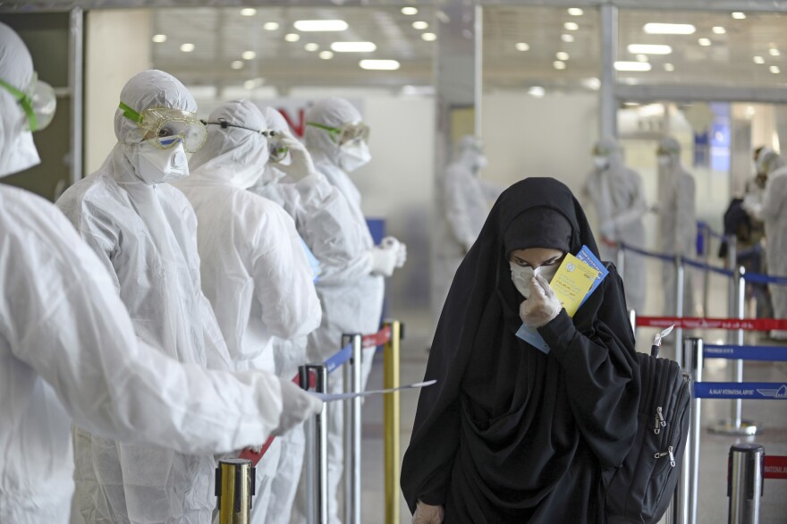 Staff in protective gear hand out information sheets about COVID-19 to Iraqi passengers returning from Iran at Najaf International Airport on March 5, 2020. Iraq was then experiencing a serious outbreak.