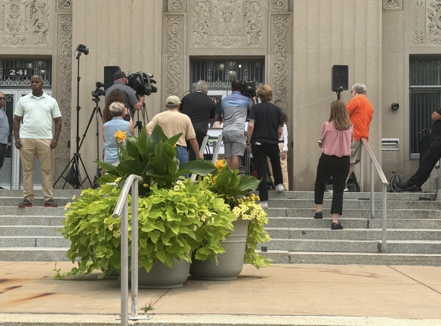 Attorney General Dana Nessel, hidden behind a crowd of reporters, speaks during a press conference on the steps of Kalamazoo City Hall on July 16, 2026.