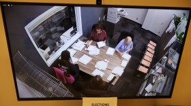 A photo of a television monitor which shows people counting ballots.