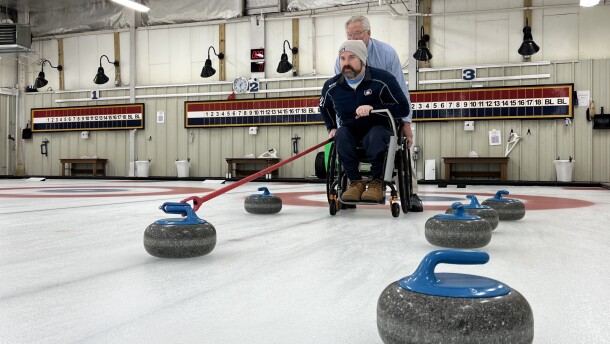 Sean O'Neill will represent the United States in the Paralympic Winter Games in Milan Cortina. Here, the Sandwich resident demonstrates the sport at his home club, the Cape Cod Curling Club in Falmouth, Dec. 19, 2025. Steadying the chair from behind — standard practice in wheelchair curling — is Doug Jones, a teammate of O'Neill's in local leagues.