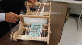 Professor Jayan Thomas shows the loom he used to weave solar ribbons into a piece of fabric