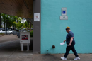 A person carrying an envelope walking on a sidewalk approaching a ballot drop box.