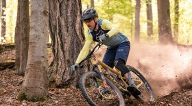 A man on a yellow bike rides through a forest, kicking up dirt behind him. 