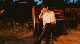 A woman sitting in front of a piano outside in the orange glimmer of the sunset.