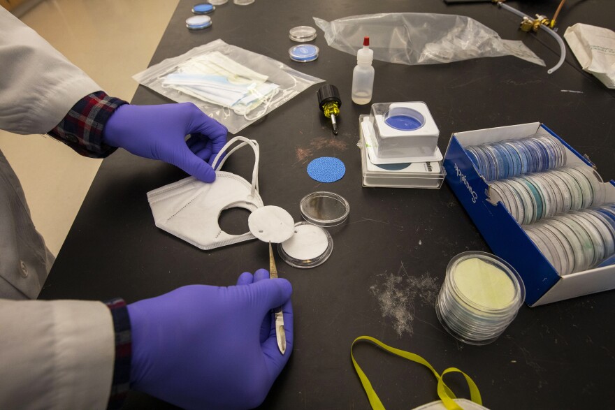 A researcher at Washington University removes a circle of material from a mask to test how well it filters tiny particles.