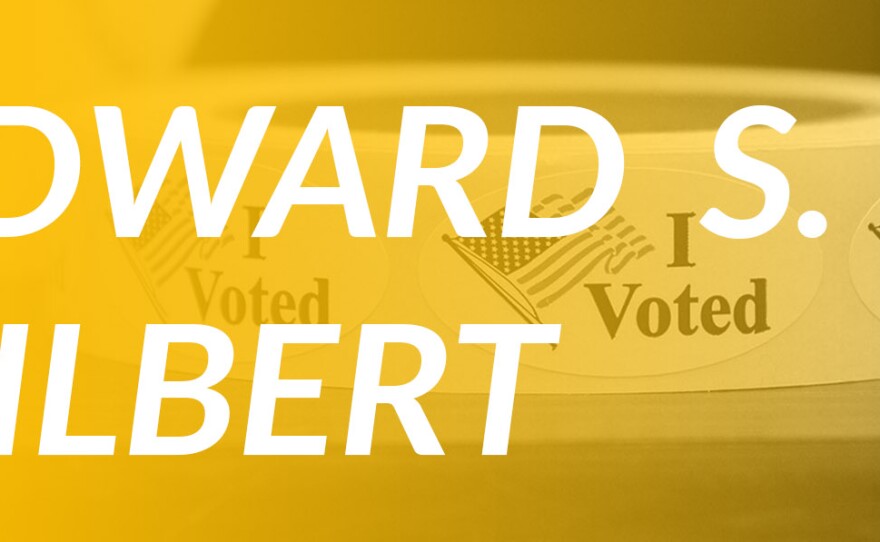 A yellow overlay over a roll of I Voted stickers with American flags and the name Edward S. Gilbert