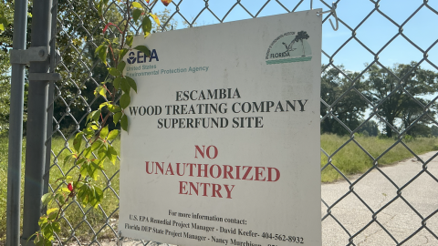 A sign marks the Escambia Wood Treating Company Superfund site, warning against unauthorized entry. The site, which is fenced and closed to the public, is the focus of ongoing environmental cleanup efforts.