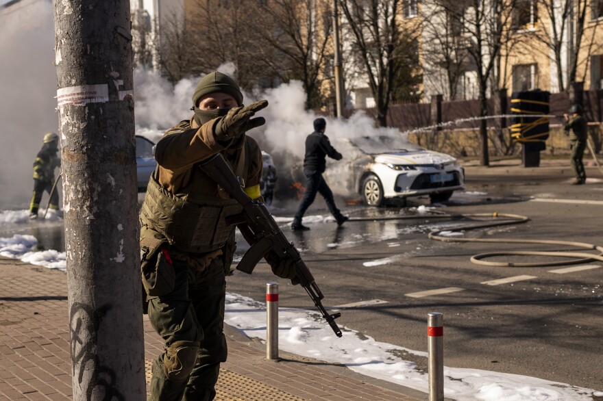 Ukrainian soldiers take positions outside a military facility as two cars burn in a street in Kyiv, Ukraine, on Saturday.