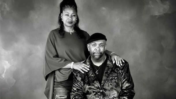 Renee Peoples stands with her hands resting on the shoulders of her seated husband, Bobby.