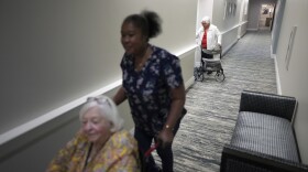 Private nursing assistant Mona Dagobert, center, pushes Eleanor Kirshner, 86, to her apartment after saying goodbye to friend Isa Medow, top, in the independent living facility at the Toby and Leon Cooperman Sinai Residences, July 4, 2025, in Boca Raton, Fla.