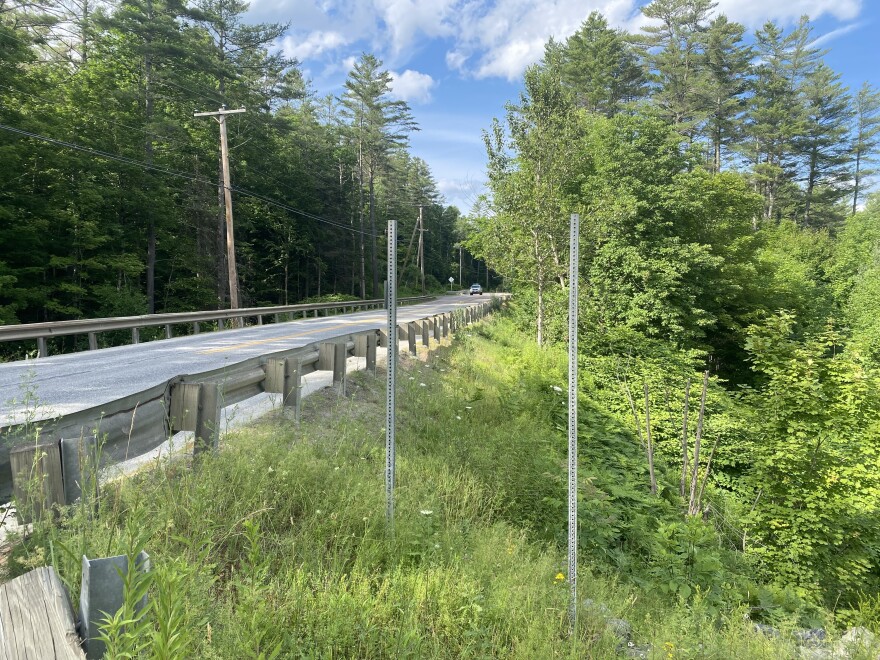 Two sign posts without a sign on top stand next to a rail by a road.