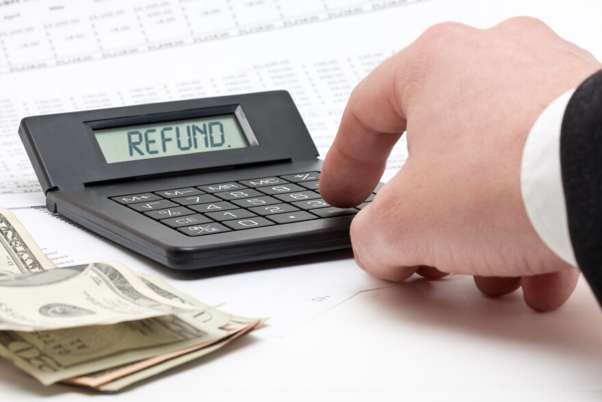 A hand types the word 'refund' into calculator with money and paperwork underneath.
