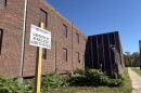 a sign on a wooden post sits in front of a brown brick building