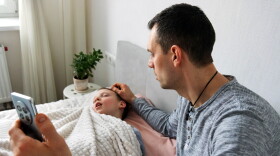 A young father worrying about his son suffering from a viral fever in their home.