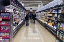 Shoppers with carts stand in a grocery store aisle, surrounded by products on both sides.