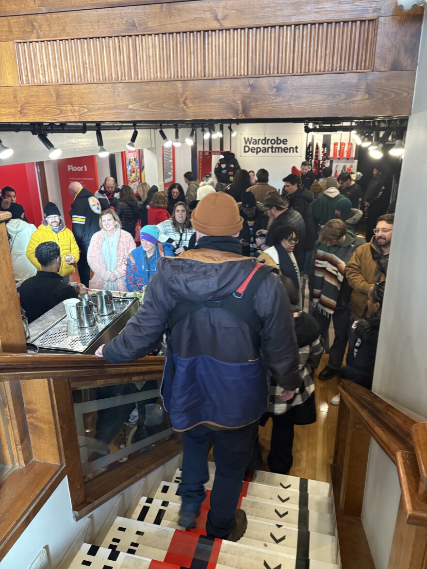 A man in a coat walks down stairs into a crowded room. 