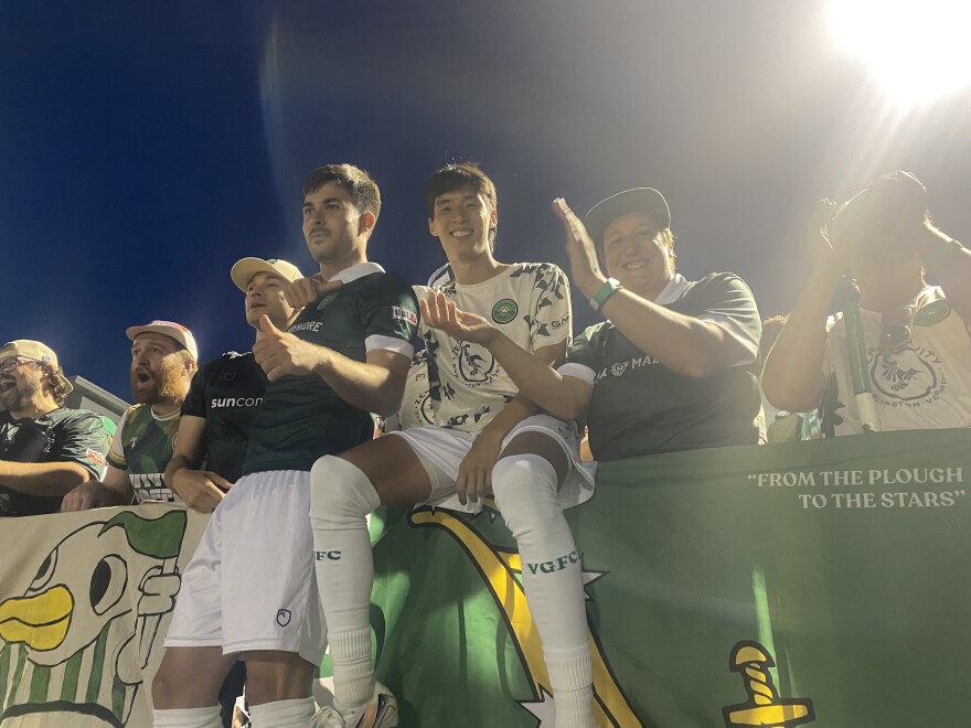 Soccer players smile and sit on the railing in the stands at Virtue Field