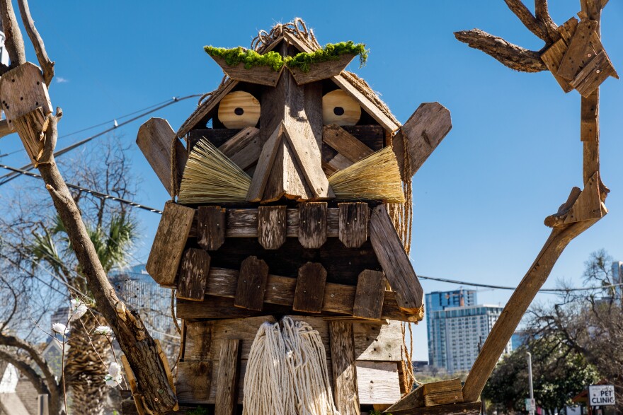 A close up of the troll, showing its large wooden face, teeth made of wooden fencing, facial hair made of mops and brooms, and eyes made of circular wooden discs.
