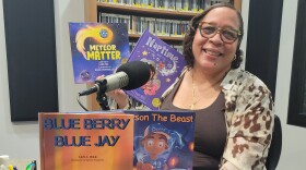 A smiling woman in a recording studio surrounded by colorful children's books