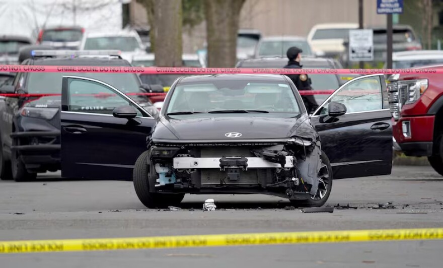 A car with visible front-end damage. Its doors are open. Yellow police tape is visible in the foreground. 