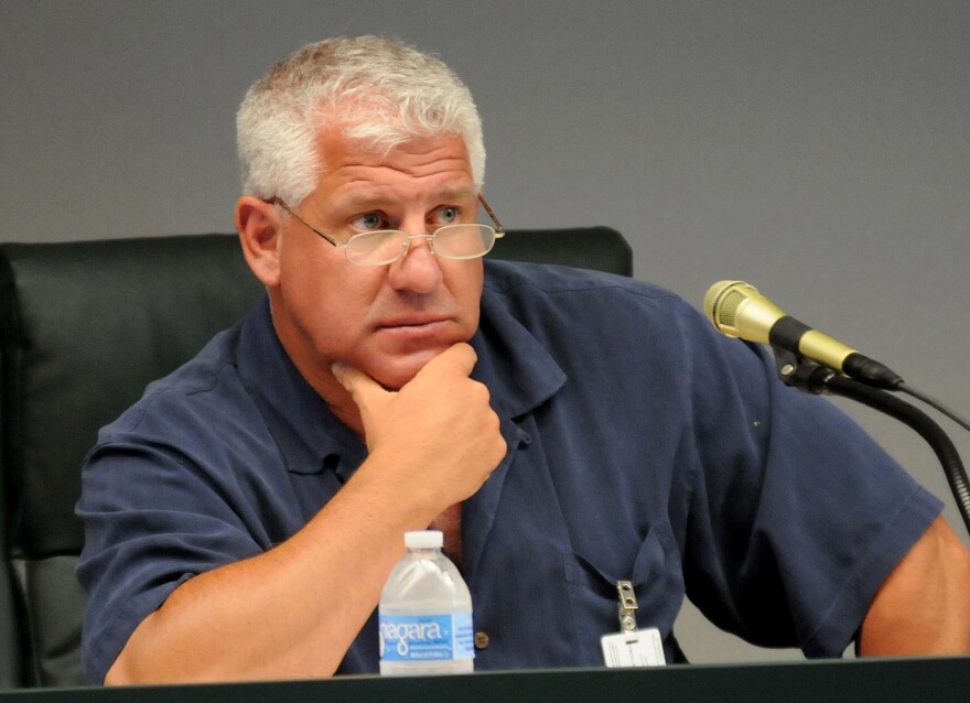 Man with white hair puts hand on chin sitting next to mic