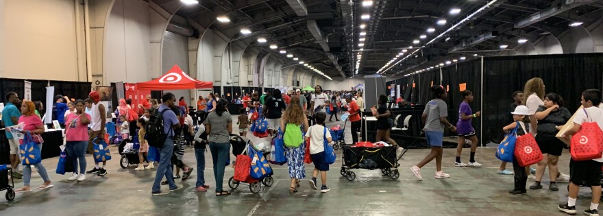 lots of families and children in a lighted warehouse, many pulling filled wagons or with large colored bags in hand or over shoulders