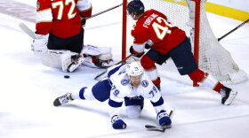 Ross Colton smiling as he falls to the ice, Panthers goalie and player in the background