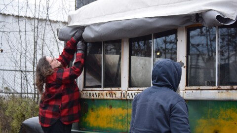 University of Alaska Museum of the North curator Angela Linn removes a tarp from Bus 142 at a storage facility in central Fairbanks on Oct 20, 2025 as visitor Jared White looks on.