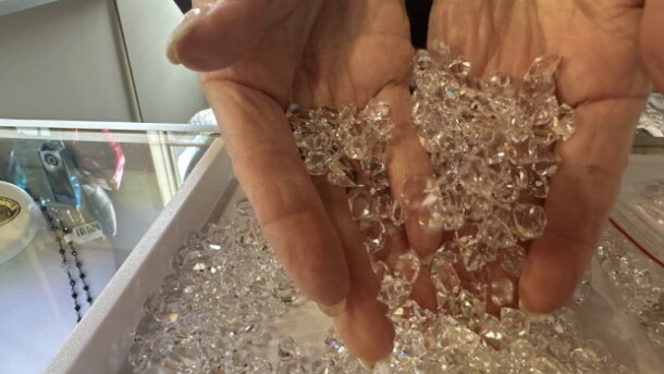 A woman's hand scoops up a tray full of diamond looking stones that are actually Herkimer Diamond quartz.