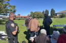 Traverse City Police Officer Matthew Kirkey and Police Support Services Worker Brad Neuder explaining the department's new enforcement efforts to a table of homeless individuals at Hull Park (Credit: IPR News / Maxwell Howard)