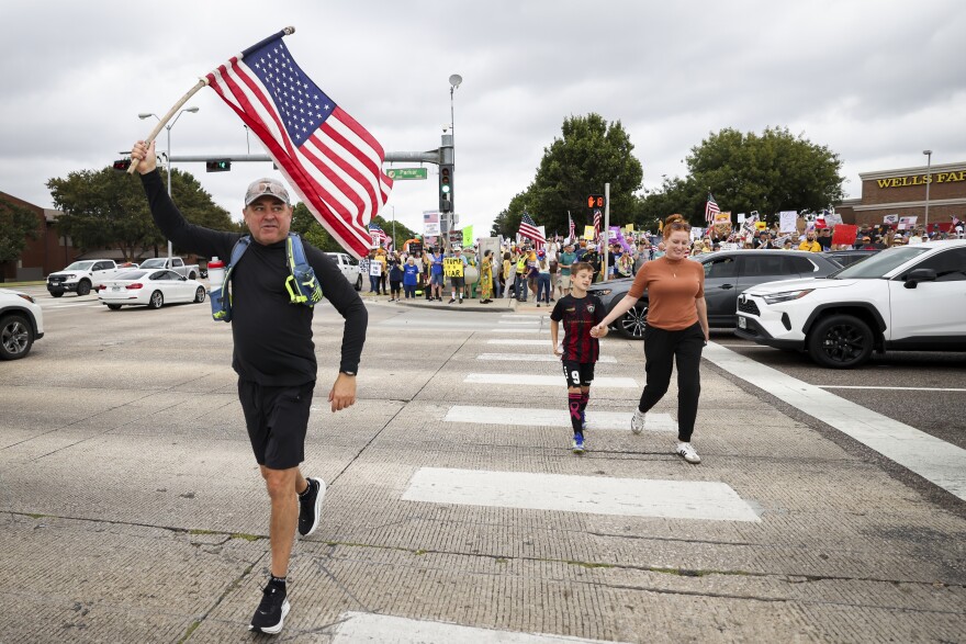 Protesters cross the street as the sidewalk fills up for the ‘No Kings” protest Saturday, October. 18, 2025, in Plano, Texas.