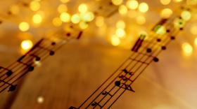 Sheet music up close adorned across the top with warm holiday string lights.