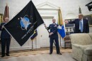 The president and two other military people stand in the oval office. One person holds a large flag that says "United States Space Force" 