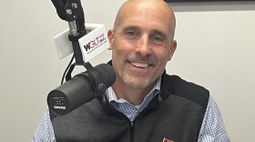 A head and shoulders image of a man wearing an Illinois State University sweater vest and small-checked shirt. He is sitting at a microphone that has a WGLT label on it.  He is Jeff Mavros, ISU Executive Director of Admissions and Recruitment Marketing