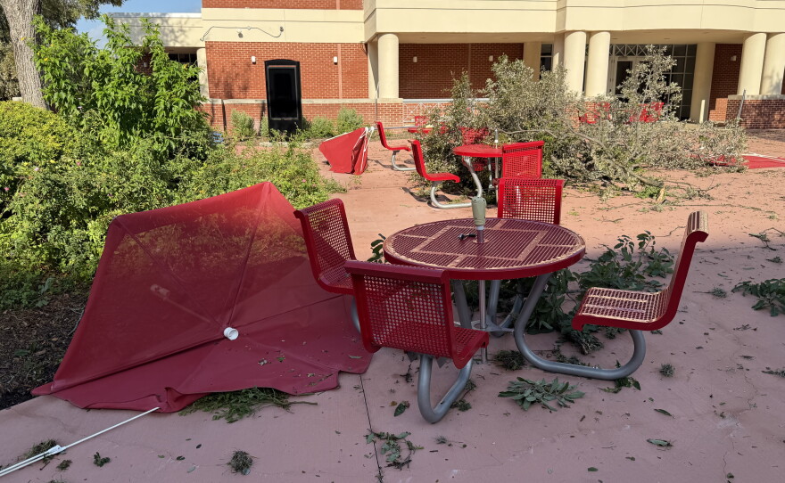 Storm debris, including a toppled patio umbrella and fallen tree limbs, is scattered across an outdoor area at San Antonio College.