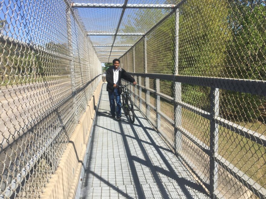 Daniel Bryant, UF English senior, walks his bike over the pedestrian walkway on NW 23rd Avenue. A sign at the entrance says “Walk Bikes Across Bridge.” A crate bottom and 20 feet separate him and his bike from traffic speeding down I-75. (Bryan Boggiano/WUFT News)