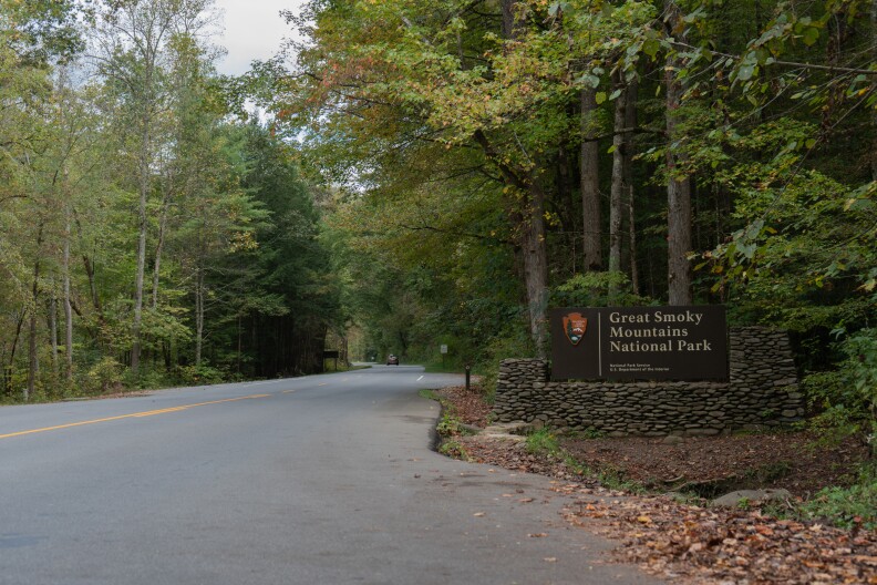 An entrance sign to Great Smoky Mountains National Park on a roadside surrounded by forest.