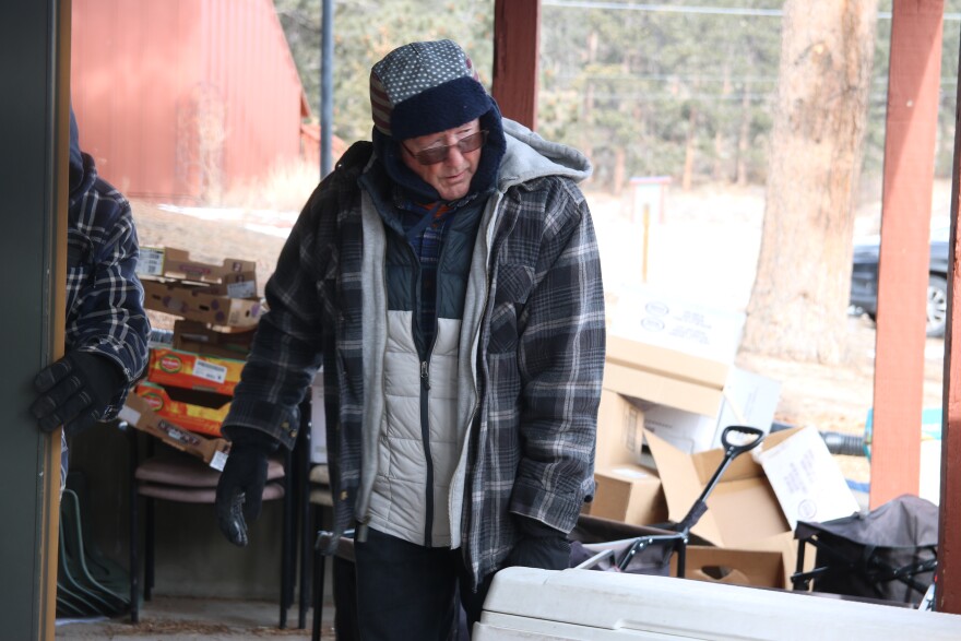72-year-old volunteer Doug Race is wearing sunglasses, a big winter coat and a fuzzy hat. He's standing in front of a white cooler.
