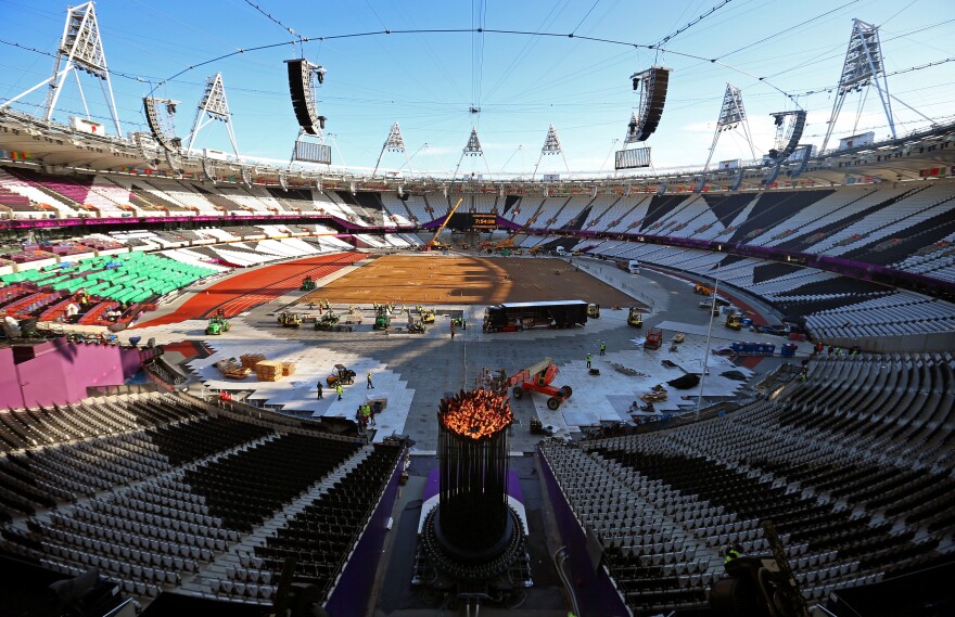 In a mostly empty Olympic Stadium, Austin Playfoot lights the Olympic cauldron Monday morning. The cauldron was extinguished Sunday night, so it could be moved to one end of the stadium. Click the enlargement to see a close-up view.