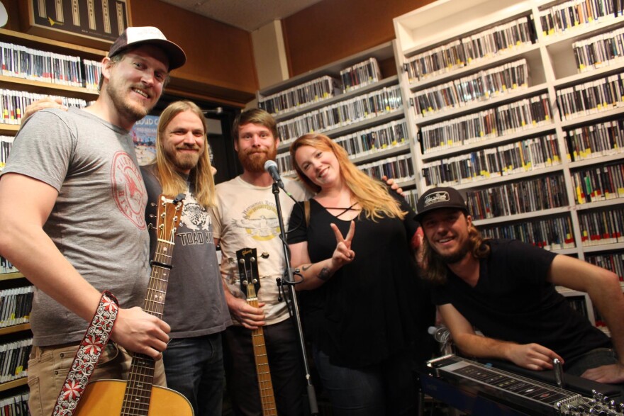 Band standing in front of wall of CDs in a radio studio