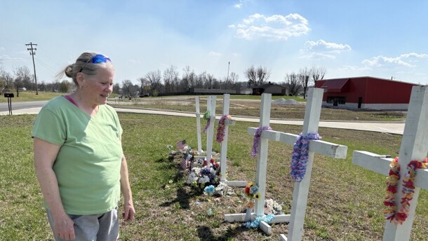 Collage artist Aleta Stone visits the white crosses put up in remembrance of those who died in the 2025 tornado. It's close to where she collected remnants for the collages that became art awards.