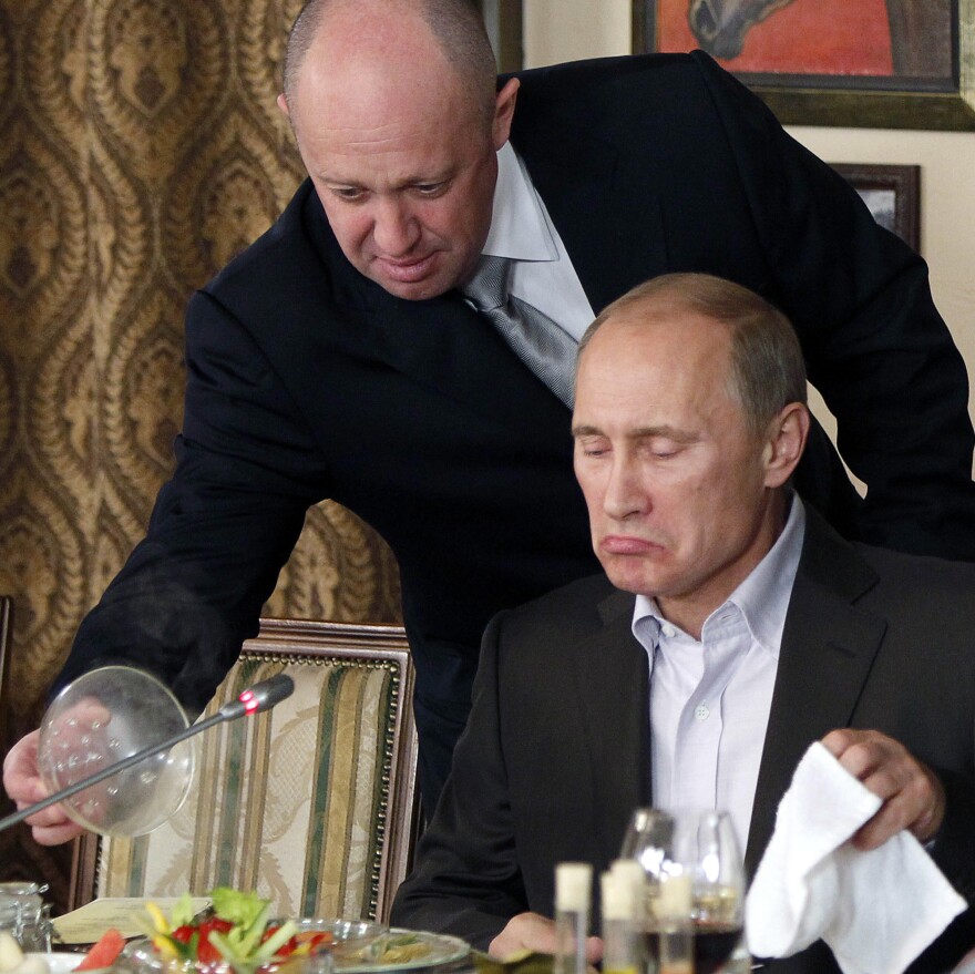 In this Nov. 11, 2011, file photo, Yevgeny Prigozhin, left, serves food to then-Russian Prime Minister Vladimir Putin during dinner at Prigozhin's restaurant outside Moscow, Russia. Friday, Prigozhin, along with 12 other Russians and three Russian organizations, was charged by the U.S. government as part of a vast and wide-ranging effort to attack the 2016 U.S. presidential election.