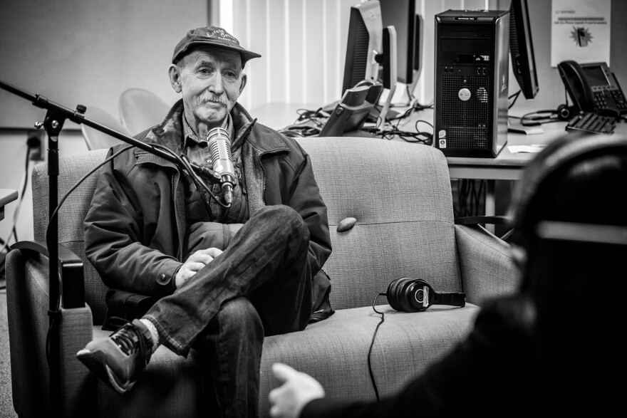 Richard Old sits in front of a microphone and smiles over to Sueann.